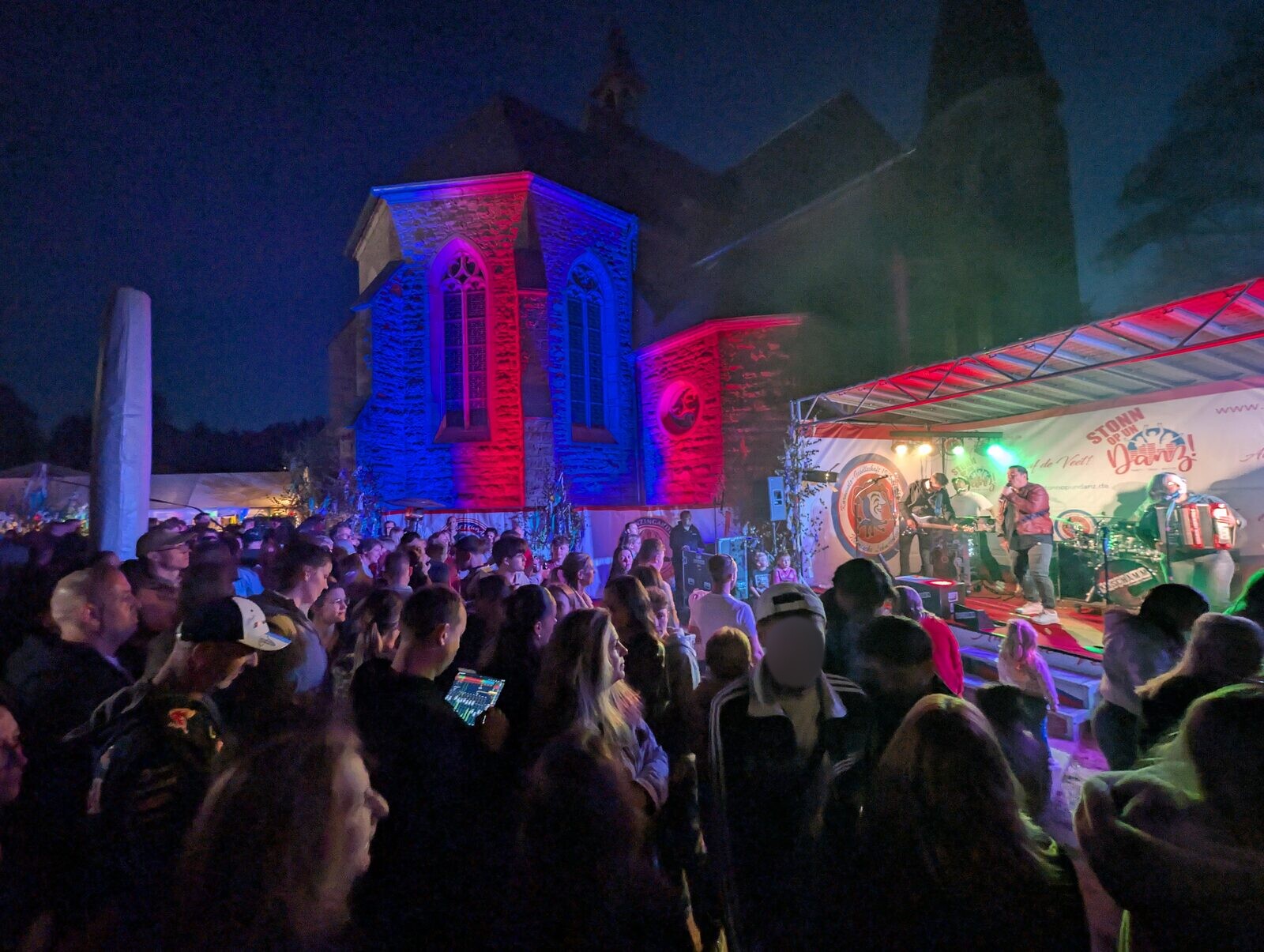 Nächtliches Open Air mit Bühnenproduktion und rot-blauem Fassadenlicht an einer Kirche